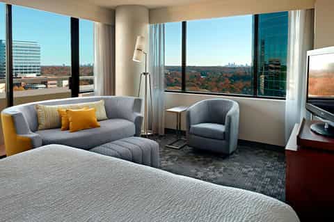 High-rise hotel room with gray sofa, panoramic windows overlooking autumn forest landscape