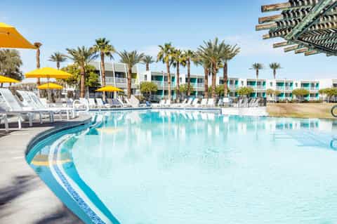 Resort pool with turquoise water, palm trees, yellow umbrellas, and modern accommodations
