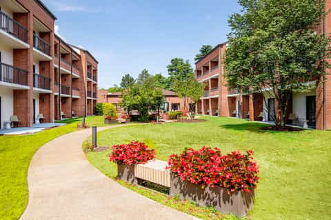 Brick residential courtyard with manicured lawn, red flowers, and curved walkway