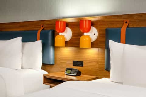 Modern hotel room with queen beds, wood headboard, orange and yellow wall sconces, white bedding