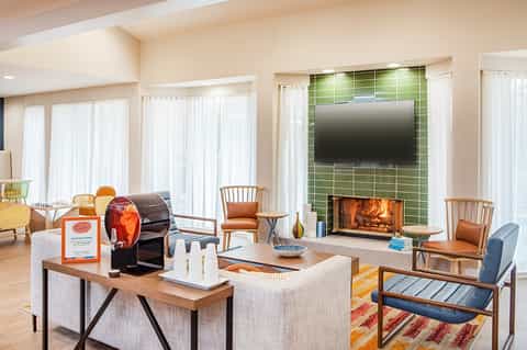 Modern living room with fireplace, green tile surround, wooden chairs, large windows, and contemporary furnishings