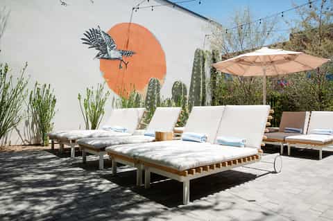 Contemporary poolside lounge with white cushioned chairs, orange mural, and desert landscaping