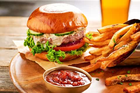 Gourmet burger with fries and ketchup served on wooden board with beverage