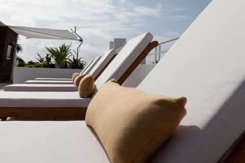 Resort rooftop lounge with white cushioned chaise lounges overlooking city skyline during daytime