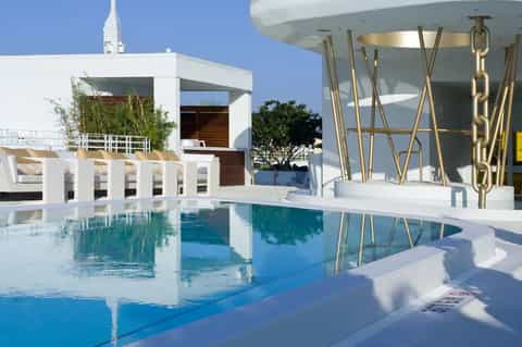 Modern resort pool with white architectural elements, gold chain details, and contemporary building design