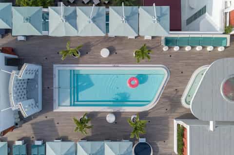 Overhead view of modern resort pool surrounded by white umbrellas, lounge areas, palm trees, and wooden decking