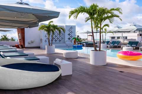 Rooftop pool deck with multiple pools, white loungers, palm trees, umbrellas, and colorful inflatables