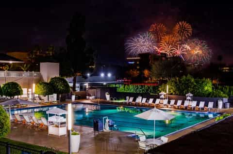 Illuminated resort pool at night with fireworks bursting in dark sky