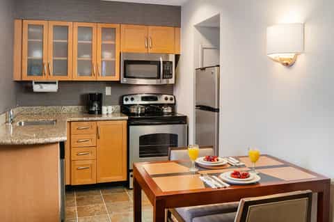 Hotel kitchenette with wooden cabinets, stainless steel appliances, granite countertop, and dining table