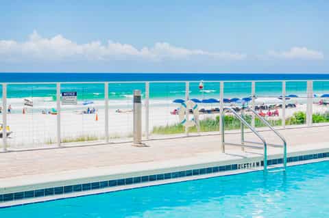 Outdoor swimming pool with ocean view and beach access behind white safety fencing