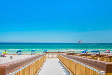 Wooden boardwalk leading to a pristine beach with colorful umbrellas and turquoise ocean waters
