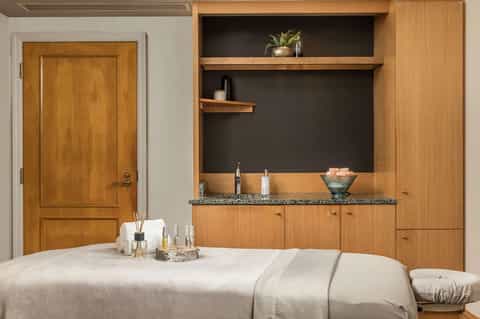 Spa treatment room with massage table, wooden storage cabinets, and grooming products