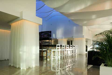 Modern resort bar interior with white sculptural elements, curved ceiling, and tropical plants