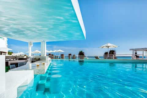 Luxury rooftop infinity pool overlooking turquoise sea with white sail shade and umbrellas