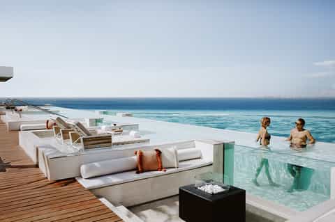 Luxury oceanfront infinity pool with modern loungers, ocean views, and guests swimming in shallow water