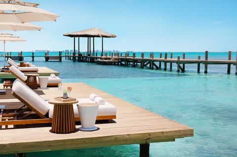 Luxury overwater bungalow with wooden deck, lounge chairs, and turquoise lagoon with thatched gazebo