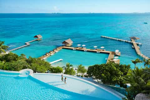 Overwater resort with thatched bungalows, turquoise lagoon, wooden docks, and infinity pool in foreground