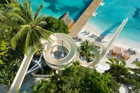 Aerial view of overwater spa with circular white pools, beach loungers, dock, and turquoise tropical waters