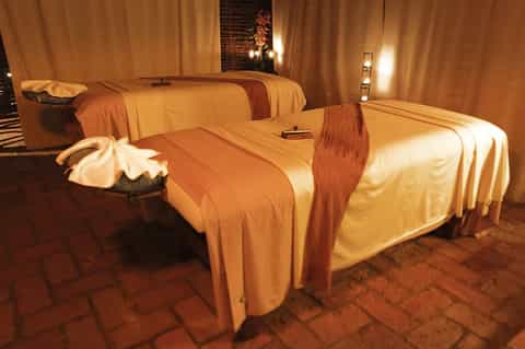 Luxurious spa treatment room with golden drapes and massage beds lit by warm lighting