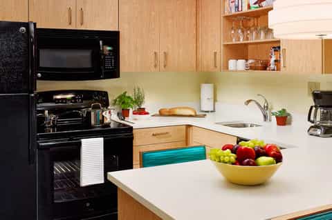 Kitchen interior with wooden cabinets, black appliances, and white countertops with fruit bowl
