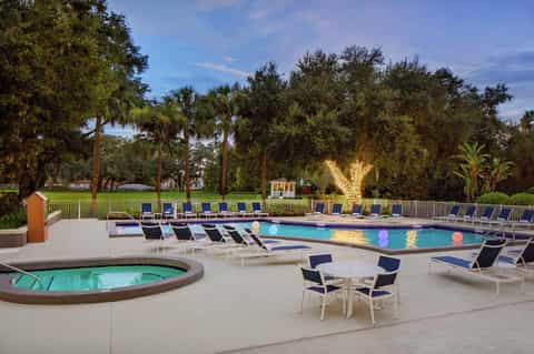 Resort pool at dusk with spa tub, loungers, and illuminated trees in background
