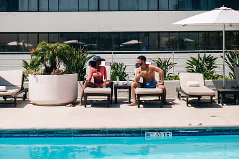Contemporary pool deck with white lounge chairs, white umbrella, large planters, and modern building
