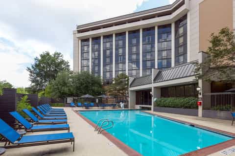 Hotel outdoor pool with blue lounge chairs, modern building facade, and manicured landscaping