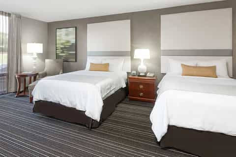 Twin hotel bedroom with white bedding, gold accent pillows, side tables, lamps, and gray accent wall