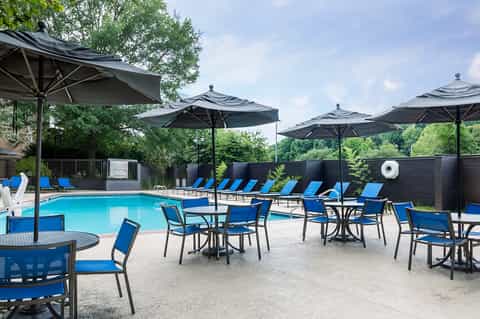 Resort pool with blue lounge chairs, black umbrellas, and tree-lined setting