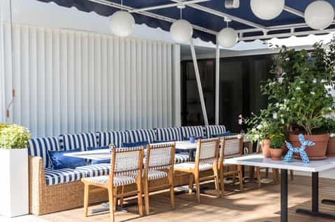 Contemporary terrace lounge with navy striped seating, pendant lighting, potted plants, and retractable shade