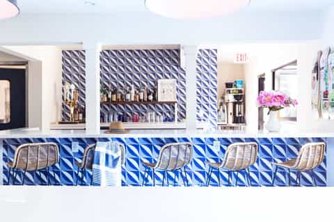 Contemporary bar with blue geometric tile pattern, white rattan stools, and shelved liquor display