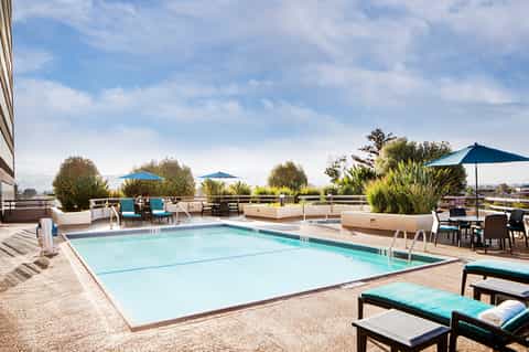 Rooftop pool with turquoise umbrellas, lounge chairs, landscaping, and city views