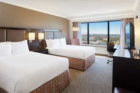 Hotel room with two queen beds, floor-to-ceiling windows, and expansive city landscape views