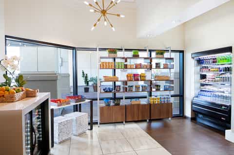 Contemporary hotel cafe with shelving, refrigerated displays, food counter, and potted plants