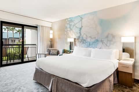 Modern hotel bedroom with king bed, balcony, and abstract headboard art