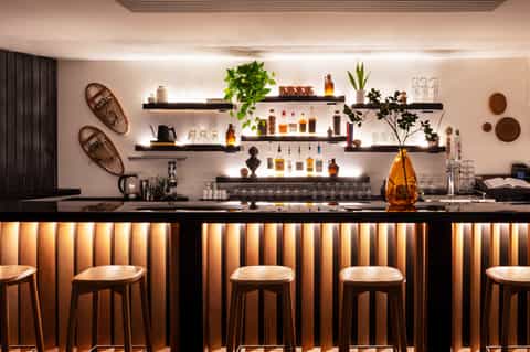 Modern spa bar with black counter, wooden stools, and illuminated shelving display