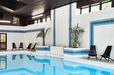 Modern indoor pool with white tile walls, blue accents, and black lounge chairs