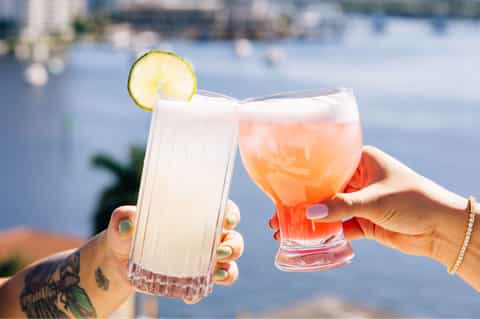 Two people toasting with tropical cocktails overlooking the waterfront