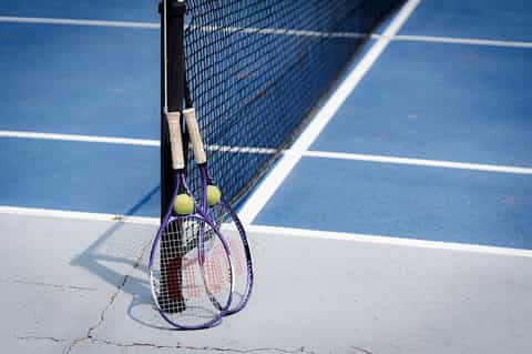 Purple tennis racket and ball leaning on net at blue tennis court