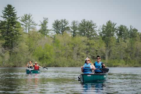 Family canoeing on a calm lake surrounded by green forest and evergreen trees