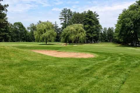Golf course fairway with sand bunker, manicured green grass, and mature shade trees lining course