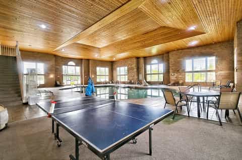 Spacious recreation room with exposed wood beam ceiling, multiple ping pong tables, and brick walls.