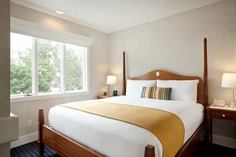 Bright bedroom with queen bed, wood headboard, large windows overlooking trees, and warm neutral tones