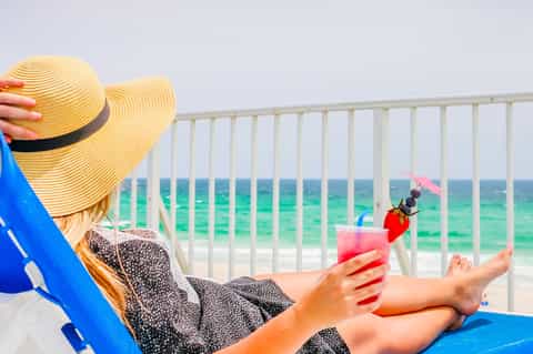 Woman in straw hat relaxing in beach chair holding tropical cocktail with ocean view
