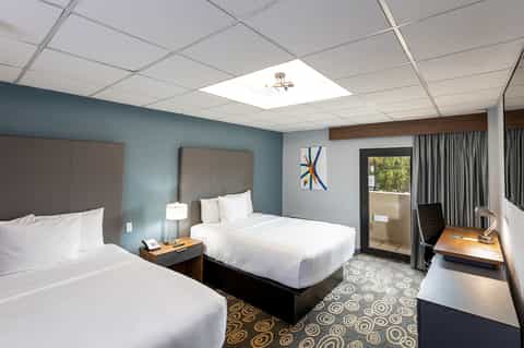 Hotel room with two queen beds, blue walls, desk area, and sliding glass door