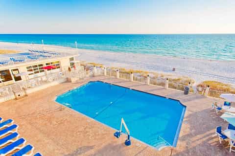 Beachfront resort pool with blue water, white lounge chairs, and ocean view beyond sandy beach