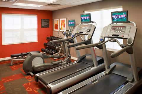 Fitness room with treadmills, elliptical machines, dumbbells, and red accent wall