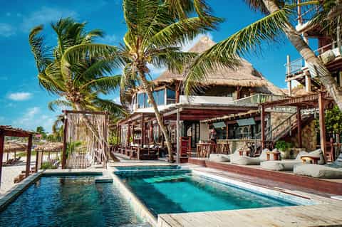 Luxury beach villa with thatched roof, private turquoise pool, palm trees, and ocean access