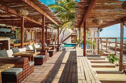 Wooden beachfront pavilion with lounge seating, palm trees, and ocean view at tropical resort
