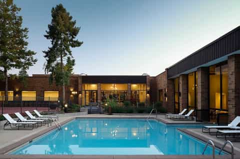 Twilight view of resort pool with lounge chairs, illuminated windows, and brick building facades